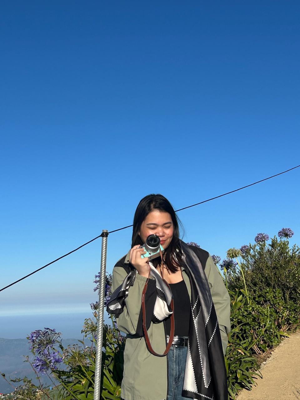 Thressia taking a photo with a camera on a mountain lookout